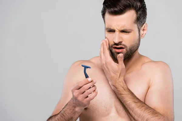 Displeased man looking at razor isolated on grey — Stock Photo