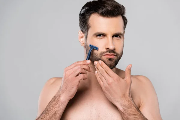 Hombre guapo sosteniendo la afeitadora mientras se afeita aislado en gris - foto de stock