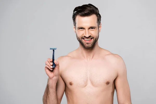 Handsome man holding razor while smiling isolated on grey — Stock Photo