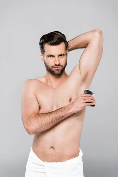 Hombre barbudo y musculoso aplicando desodorante de palo sólido aislado en gris - foto de stock