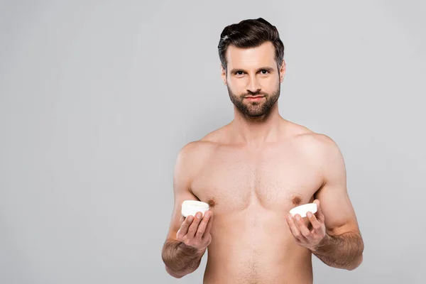 М'язистий чоловік тримає тару з косметичним кремом ізольовано на сірому — стокове фото