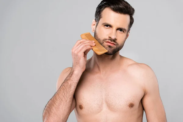 Muscular man brushing beard with comb isolated on grey — Stock Photo