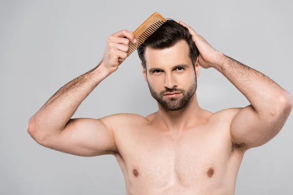 Homem muscular e barbudo escovação cabelo isolado em cinza — Fotografia de Stock