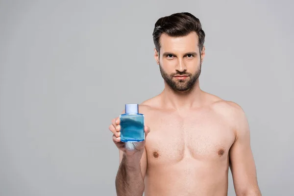 Homme musclé tenant bouteille avec lotion bleue après rasage isolé sur gris — Photo de stock