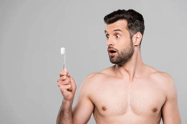 Uomo sorpreso e muscoloso guardando spazzolino isolato su grigio — Foto stock