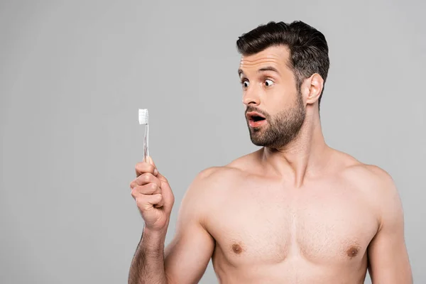 Hombre sorprendido y musculoso mirando cepillo de dientes aislado en gris — Stock Photo