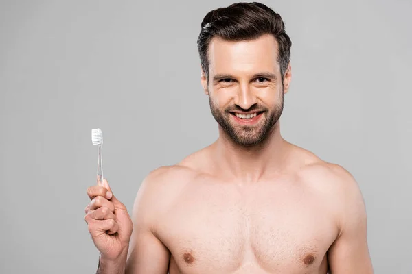 Homem alegre e muscular segurando escova de dentes isolado em cinza — Fotografia de Stock