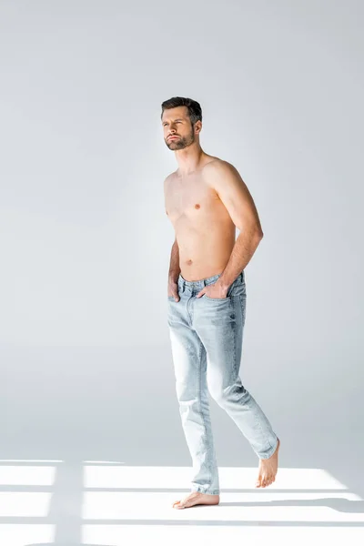 Sunshine on shirtless man in blue jeans walking with hands in pockets on grey — Stock Photo