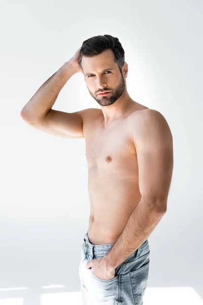 Shirtless man in blue jeans standing with hand in pocket and touching hair on white — Stock Photo