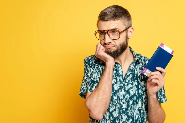 Sad bearded guy in glasses with air ticket and passport on yellow — Stock Photo