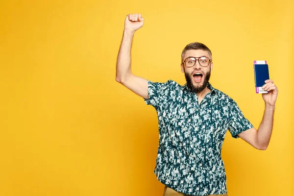 Excited bearded guy in glasses with air ticket and passport on yellow — Stock Photo