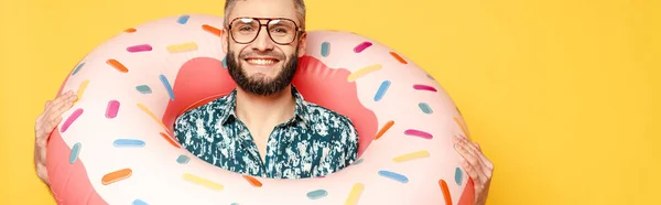 Cara barbudo sorridente em óculos com anel de natação donut isolado em amarelo, orientação panorâmica — Fotografia de Stock