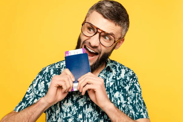 Loco barbudo chico en gafas comer pasaporte y billete aislado en amarillo - foto de stock