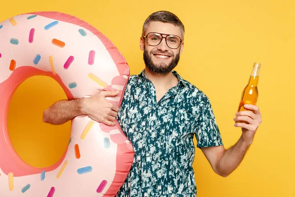 Smiling bearded guy in glasses with donut swim ring and beer on yellow — Stock Photo