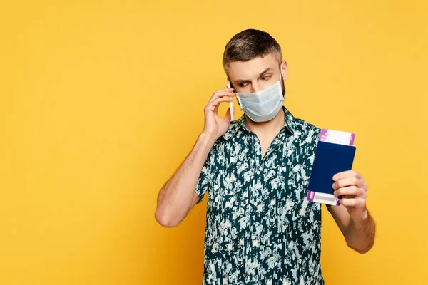 Guy in medical mask with passport talking on smartphone on yellow — Stock Photo