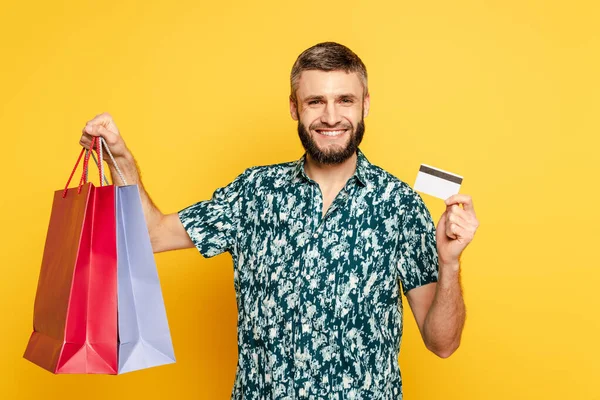 Happy bearded guy with shopping bags and credit card on yellow — Stock Photo