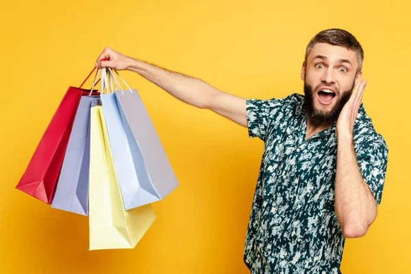 Chico barbudo feliz y sorprendido con bolsas de compras en amarillo - foto de stock