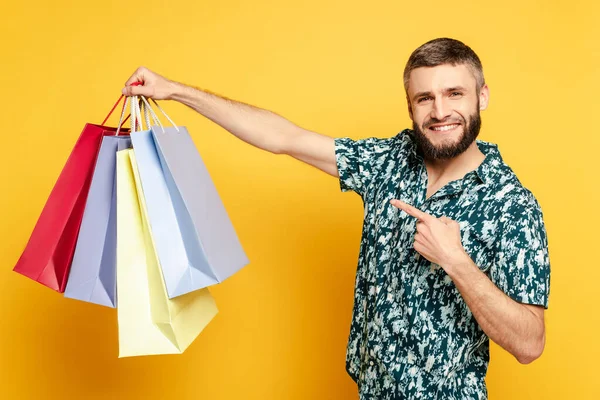 Feliz barbudo chico apuntando a las bolsas de compras en amarillo - foto de stock