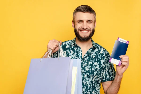 Happy bearded guy with shopping bags and passport isolated on yellow — Stock Photo