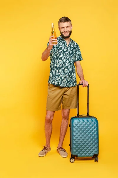 Повний вигляд щасливого бородатого хлопця з дорожньою сумкою і пивом на жовтому — стокове фото