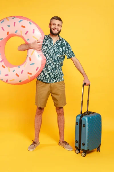 Повний вигляд щасливого бородатого хлопця з дорожньою сумкою і плаваючим кільцем на жовтому — стокове фото