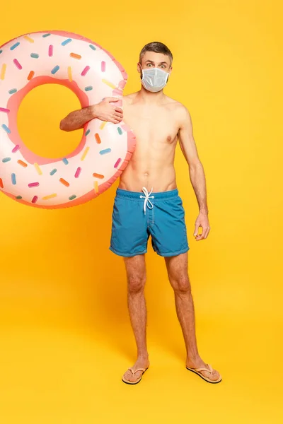 Full length view of guy in swim trunks and medical mask with swim ring on yellow — Stock Photo