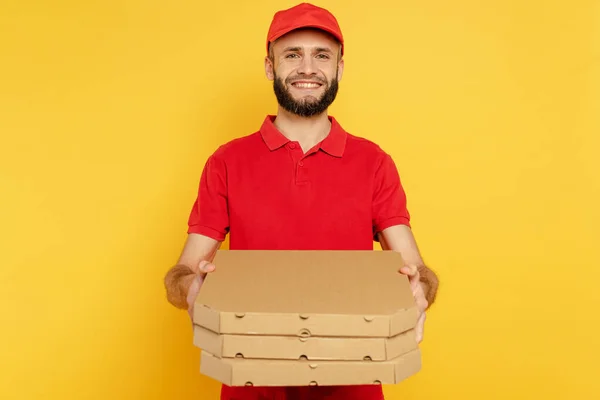 Lächelnder bärtiger Zusteller in roter Uniform mit Pizzakartons auf gelb — Stockfoto