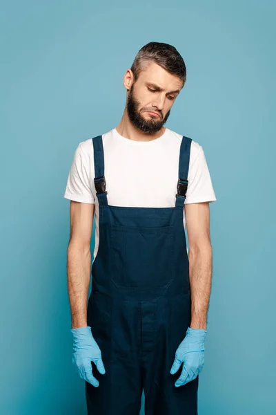 Limpiador triste en uniforme y guantes de goma sobre fondo azul - foto de stock