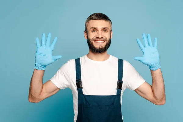 Limpador feliz em uniforme mostrando as mãos em luvas de borracha no fundo azul — Fotografia de Stock