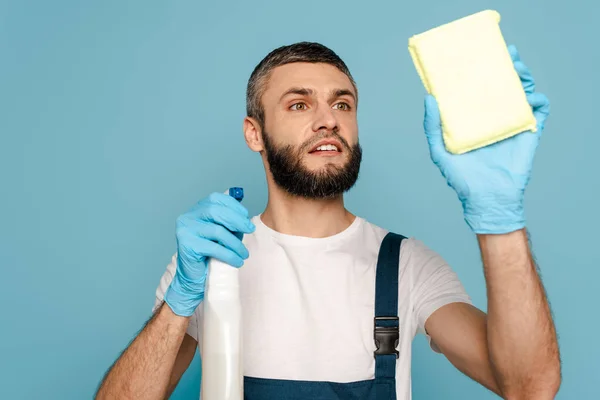 Limpiador en uniforme y guantes de goma con detergente y esponja sobre fondo azul - foto de stock