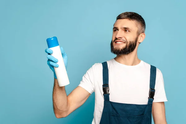 Limpador feliz em uniforme e luva de borracha segurando ambientador de ar no fundo azul — Fotografia de Stock