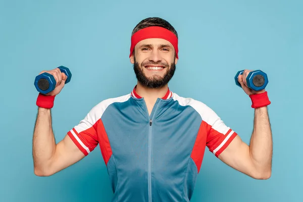 Lächelnder stilvoller Sportler, der mit Hanteln auf blauem Hintergrund trainiert — Stockfoto