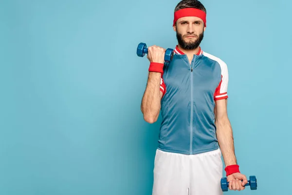 Deportista con estilo serio ejercicio con mancuernas sobre fondo azul - foto de stock