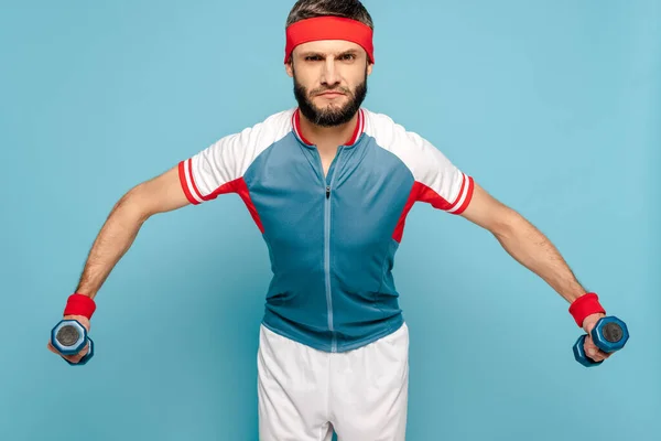 Serious stylish sportsman exercising with dumbbells on blue background — Stock Photo