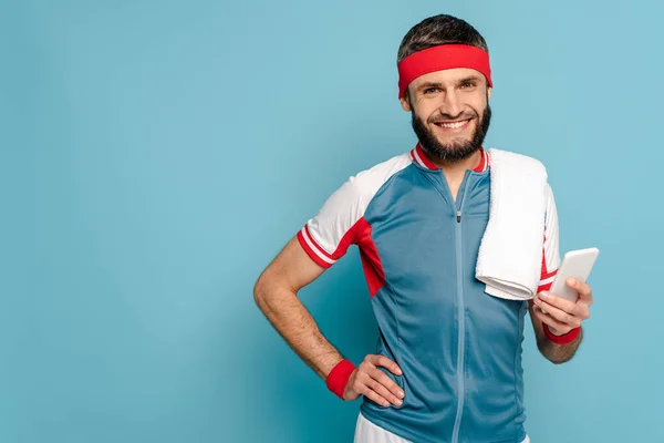 Sportif élégant souriant avec serviette en utilisant un smartphone sur fond bleu — Photo de stock