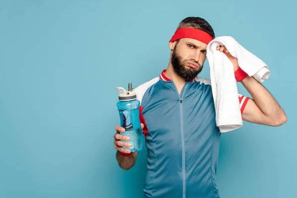 Tired stylish sportsman with towel and water on blue background — Stock Photo