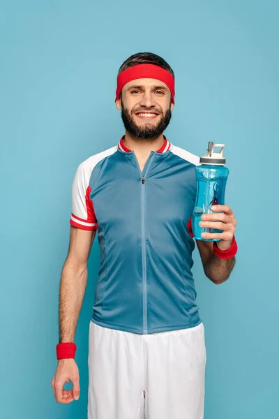 Smiling stylish sportsman with water on blue background — Stock Photo