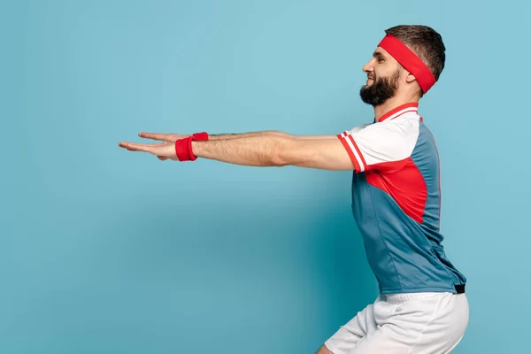 Side view of happy stylish sportsman squatting on blue background — Stock Photo
