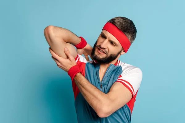 Stylish sportsman looking at biceps on blue background — Stock Photo