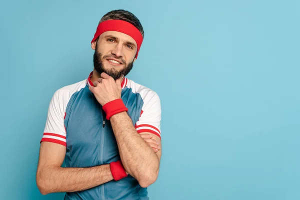 Uomo sportivo elegante sorridente toccando mento su sfondo blu — Foto stock