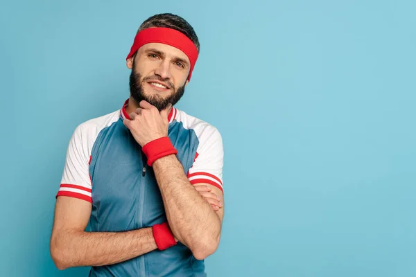 Sportif élégant souriant touchant menton sur fond bleu — Photo de stock