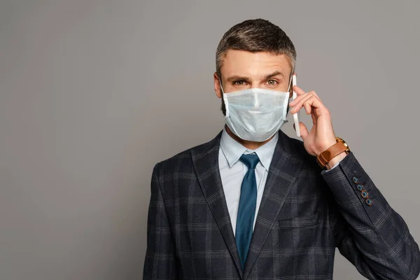 Handsome businessman in medical mask talking on smartphone on grey background — Stock Photo