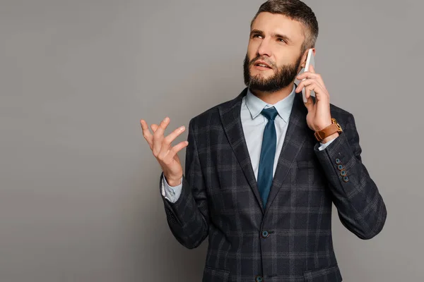 Handsome bearded businessman in suit talking on smartphone on grey background — Stock Photo