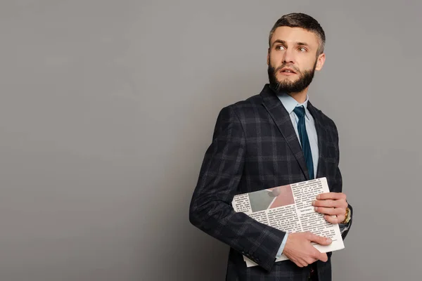 Sorridente bonito barbudo empresário em terno com jornal em fundo cinza — Fotografia de Stock