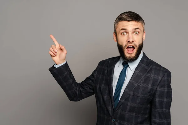 Excité homme d'affaires barbu en costume pointant du doigt sur fond gris — Photo de stock