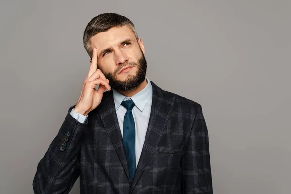 Cher homme d'affaires barbu en costume touchant temple sur fond gris — Photo de stock