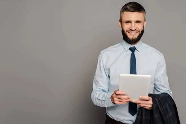 Усміхнений красивий бородатий бізнесмен з цифровим планшетом на сірому фоні — стокове фото
