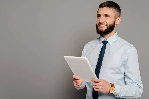 Sonriente hombre de negocios barbudo guapo con tableta digital sobre fondo gris - foto de stock