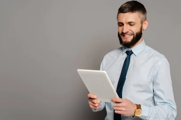 Усміхнений красивий бородатий бізнесмен з цифровим планшетом на сірому фоні — стокове фото
