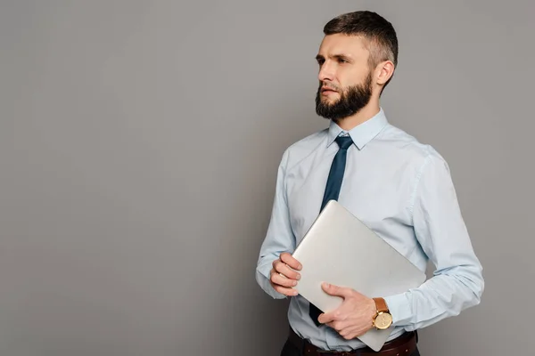 Handsome bearded businessman with laptop on grey background — Stock Photo